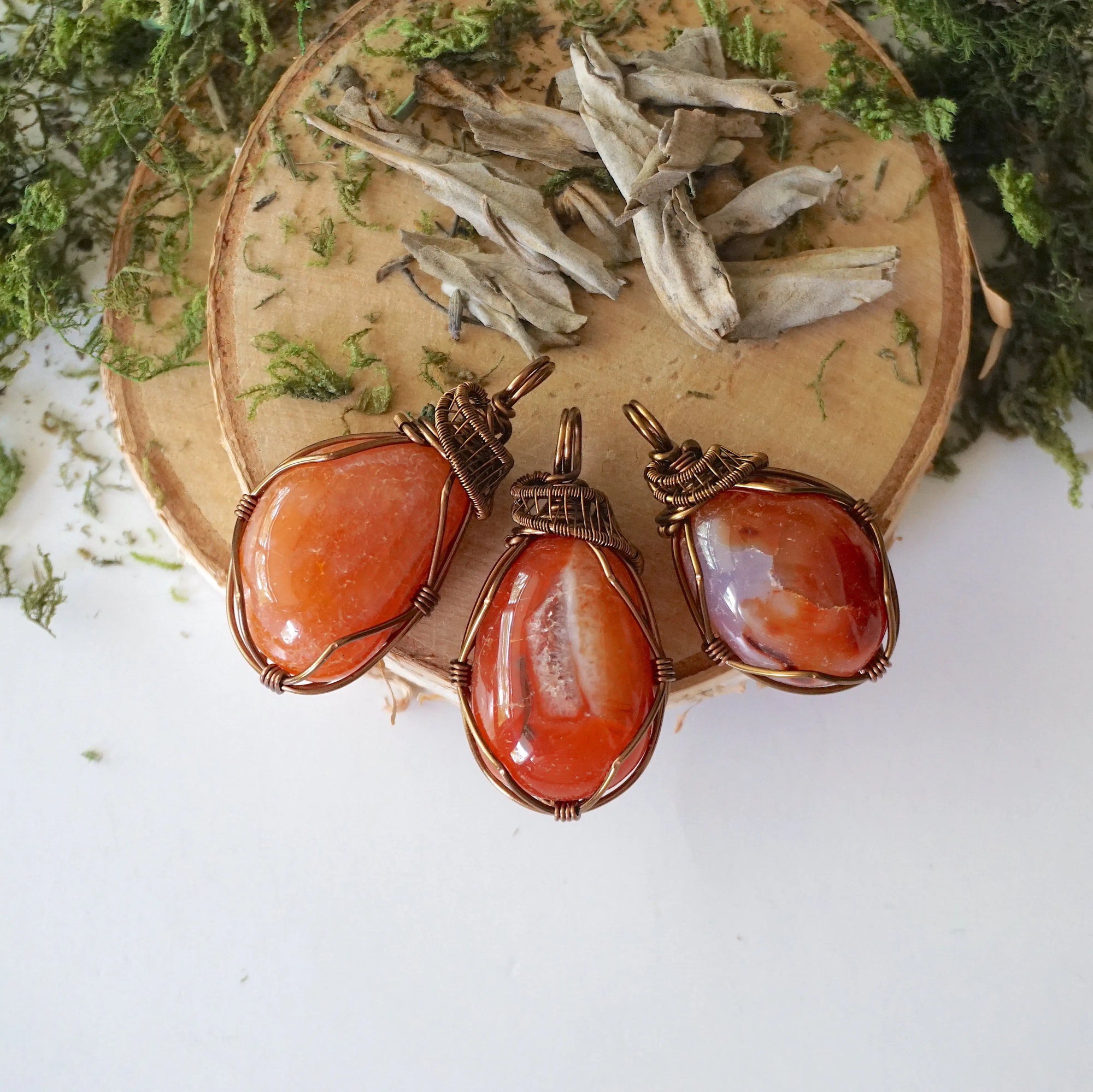 Three raw carnelian pendants – showing natural variation in size, shape, and orange shade, handcrafted unisex birthstone jewelry.