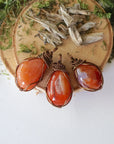 Three raw carnelian pendants – showing natural variation in size, shape, and orange shade, handcrafted unisex birthstone jewelry.