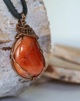 Right angle close-up of men's carnelian necklace – detailed bronze copper wire wrapping, raw carnelian, black leather cord.