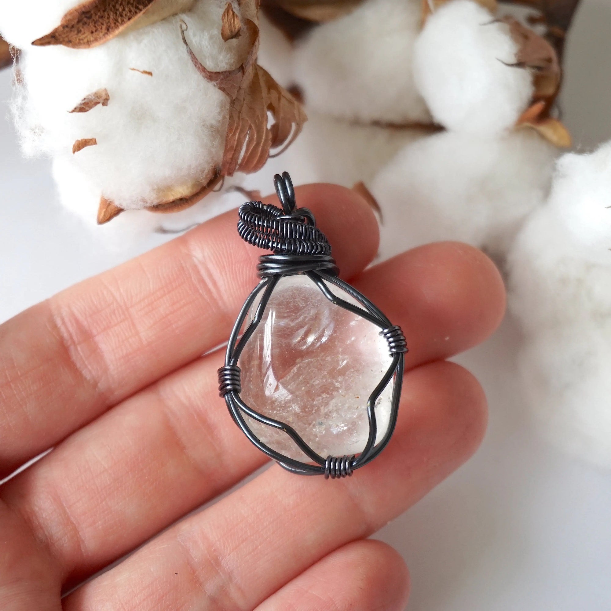 Clear quartz pendant in hand for size reference – natural polished crystal, gunmetal copper wire wrapping, April birthstone.
