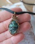 Raw emerald pendant for men shown in hand for size reference – natural green crystal, artisan wire, black leather cord.