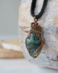 Left angle close-up of men's emerald necklace – highlighting unique wire-wrapped artistry, raw emerald, black leather cord.