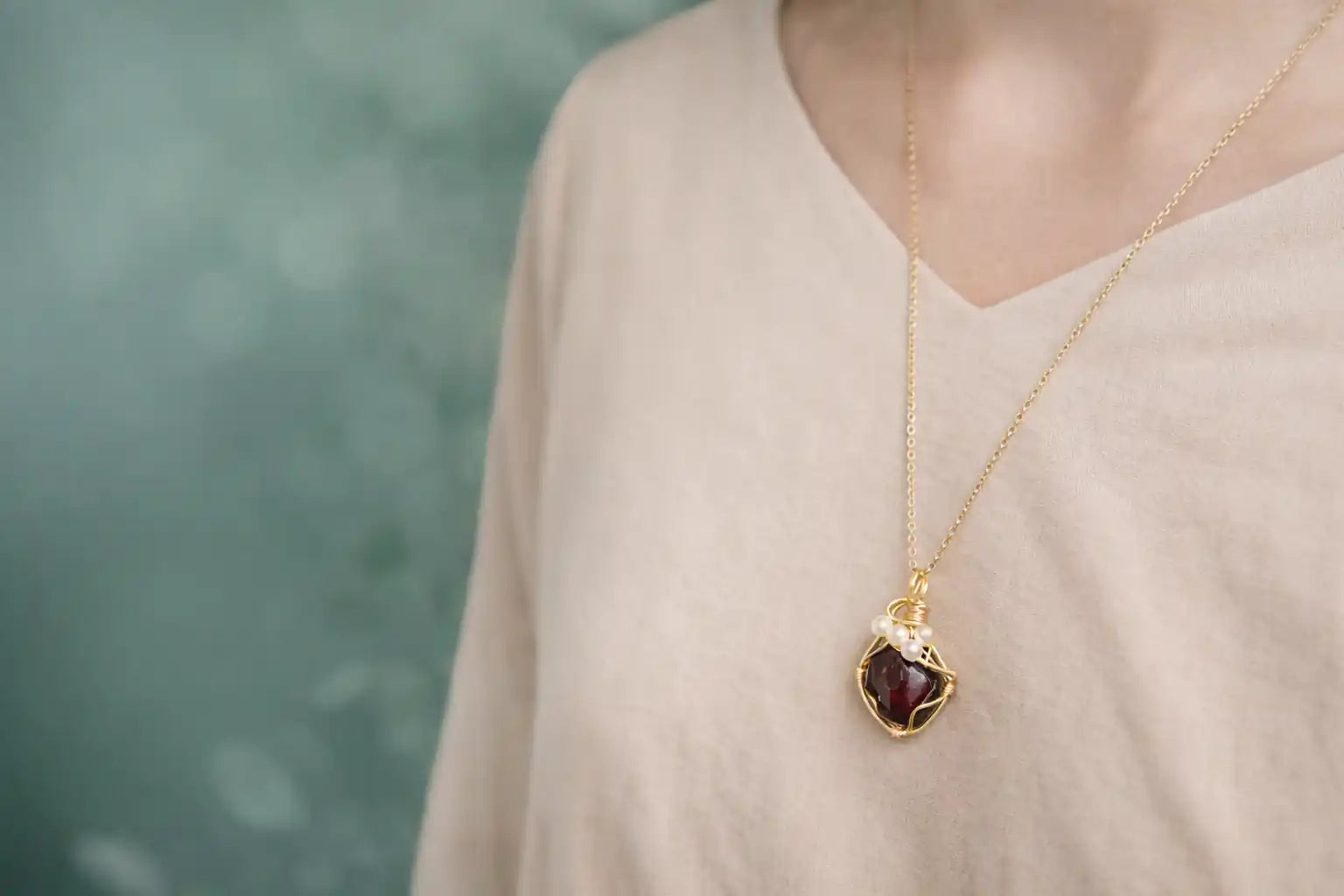 Gold necklace with a red pendant worn by a person against a blurred green background