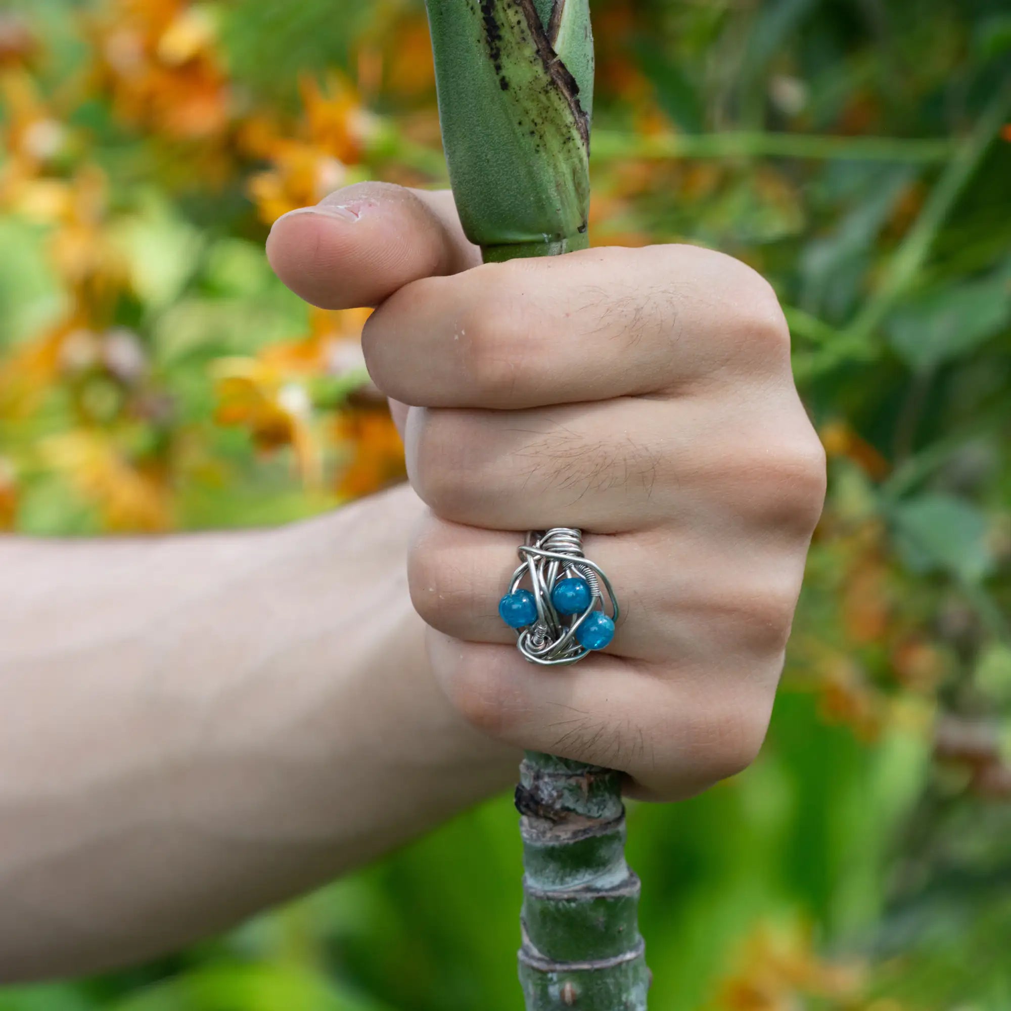 Hand holding a plant stem with a silver ring featuring blue beads.