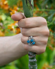 Hand holding a plant stem with a silver ring featuring blue beads.