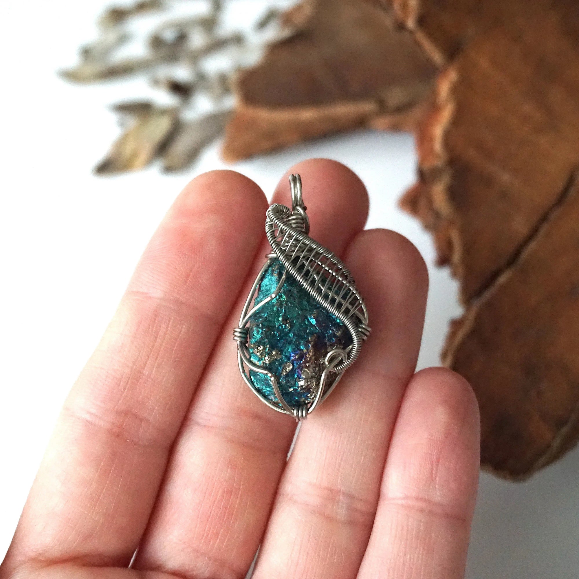 Peacock ore pendant in hand for size reference – natural raw bornite, white gold copper wire wrapping, Capricorn and Cancer birthstone, feminine design.