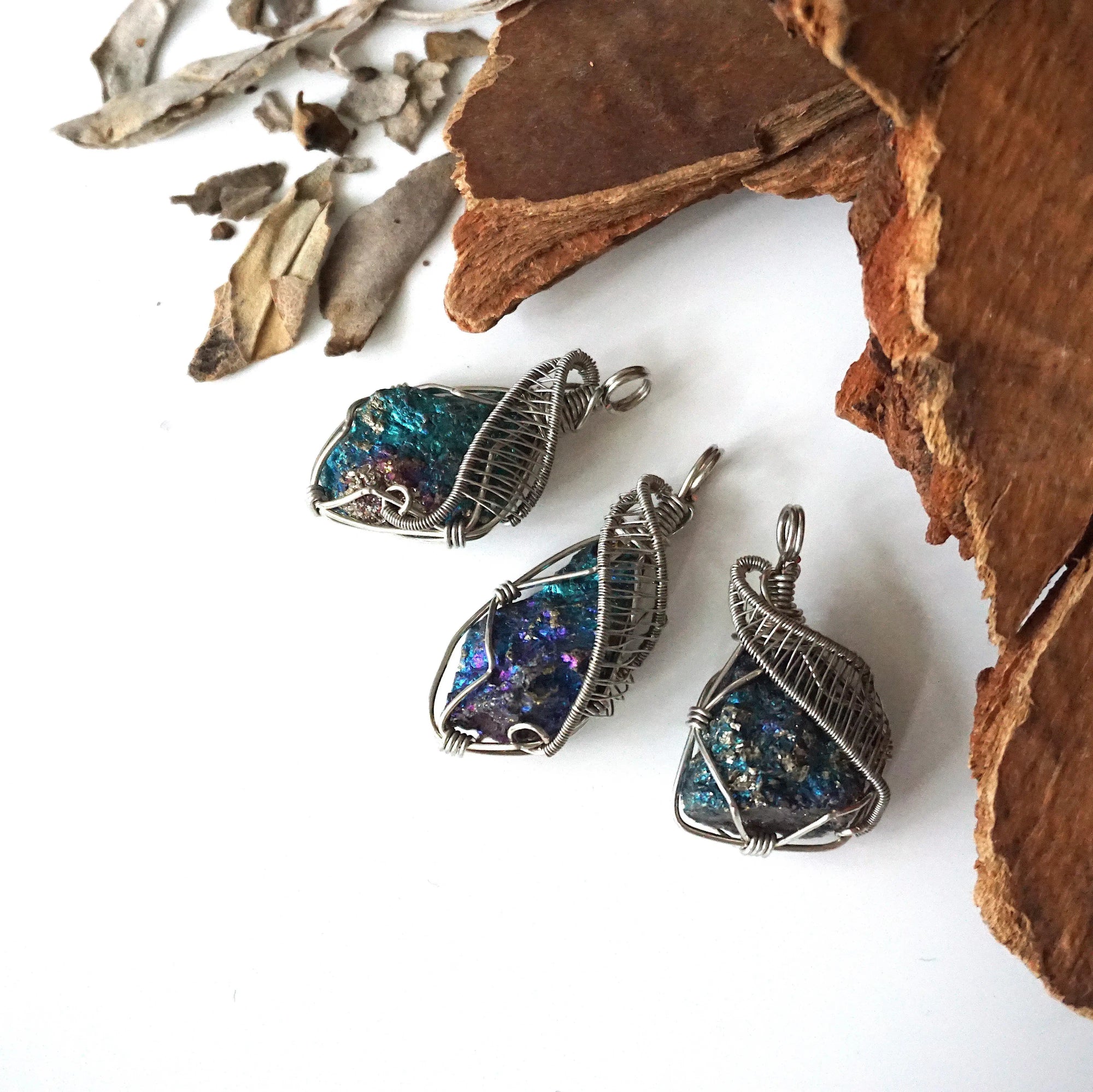 Three peacock ore pendants for women – showing natural variation in size, shape, and iridescent colours, white gold copper wire wrapping.