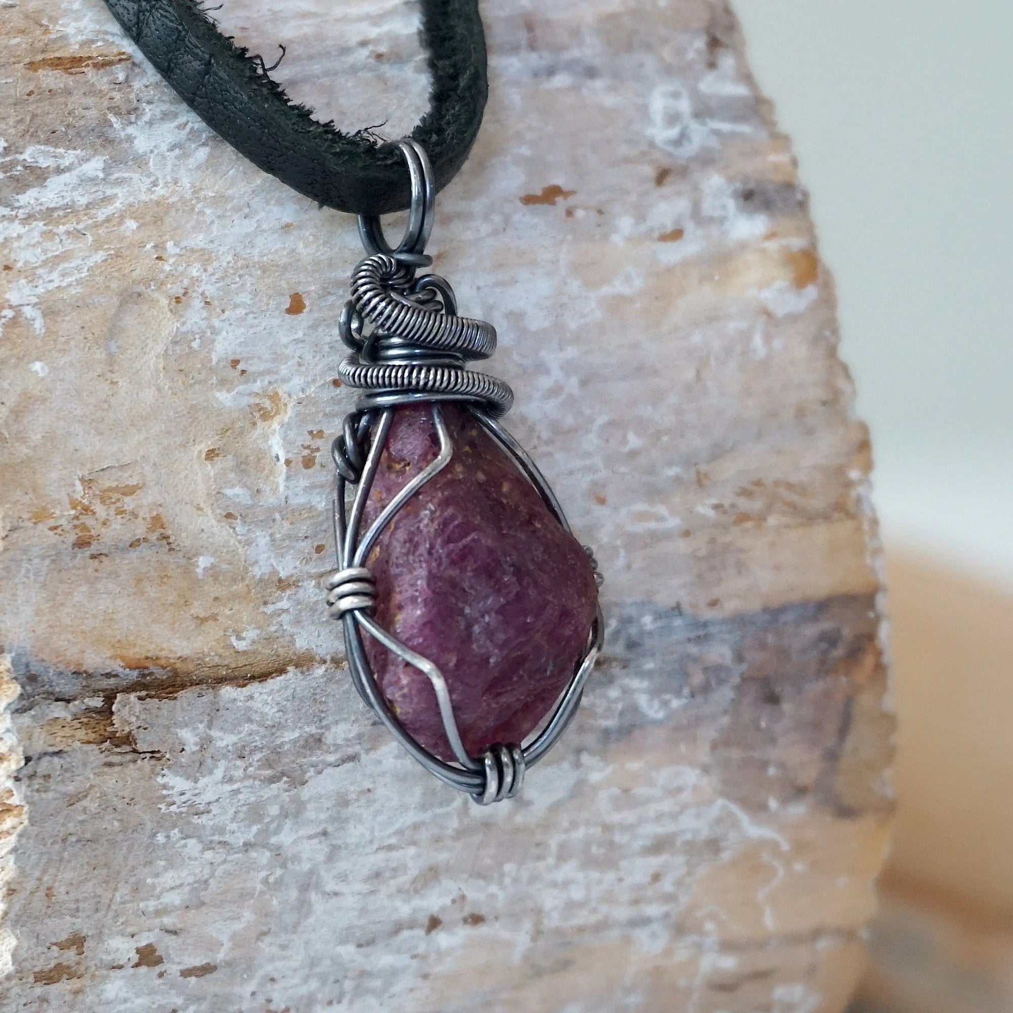 Right angle close-up of men's ruby necklace – detailed antiqued sterling silver wire wrapping, raw ruby, black leather cord.