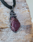 Right angle close-up of men's ruby necklace – detailed antiqued sterling silver wire wrapping, raw ruby, black leather cord.