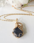 Necklace with a gold-wrapped dark blue sapphire stone pendant on a light background