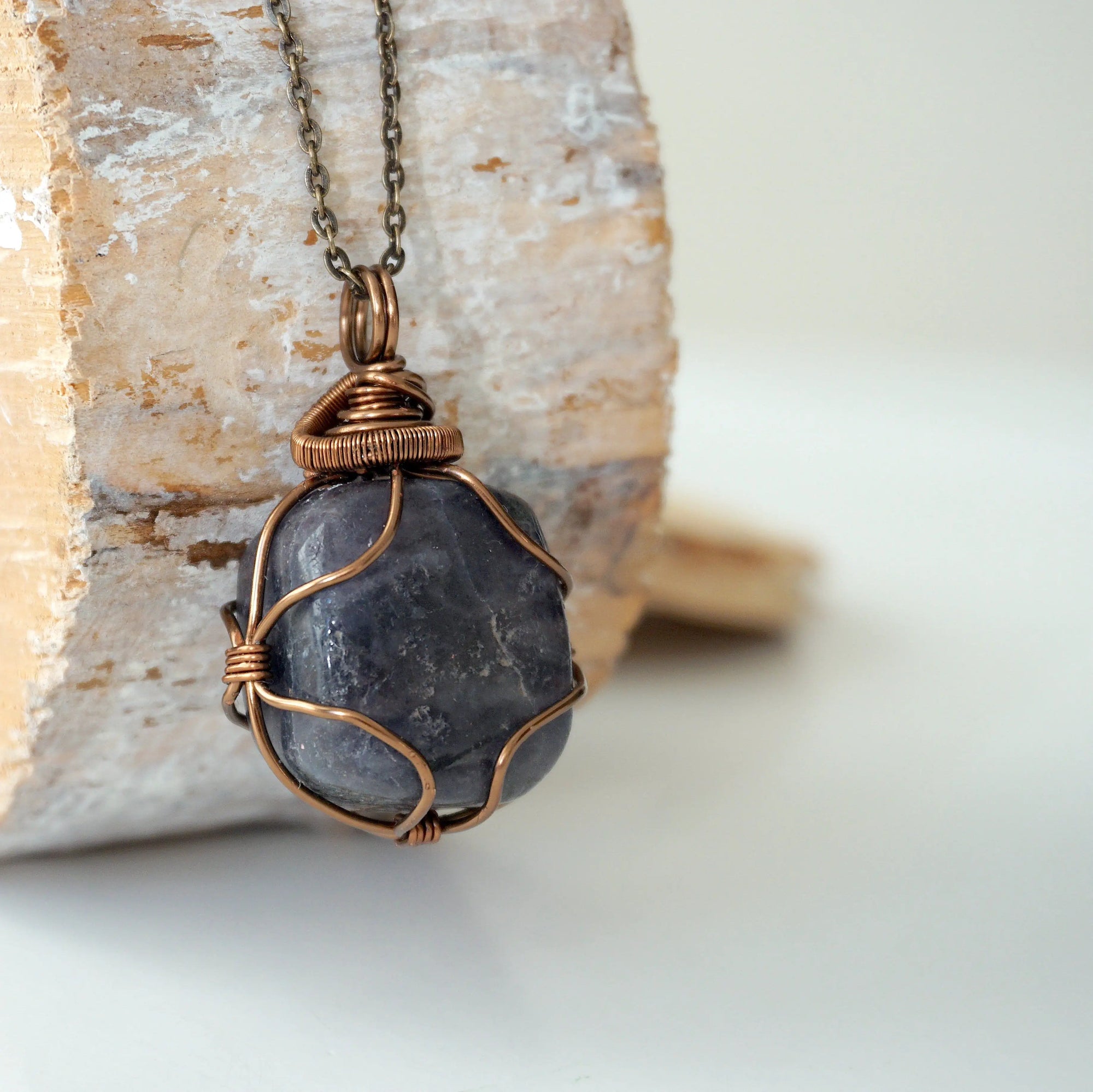 Right angle close-up of sapphire necklace – detailed artisan bronze copper wire wrapping, raw blue sapphire, handcrafted pendant.