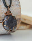 Right angle close-up of men's sapphire necklace – detailed bronze copper wire wrapping, raw blue sapphire, black leather cord.