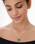 Woman wearing a silver necklace with a green pendant on a white background