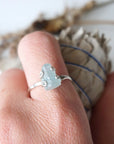 Adjustable aquamarine ring with raw gemstone in 925 sterling silver prong setting on female model's hand, Designs by Nature Gems