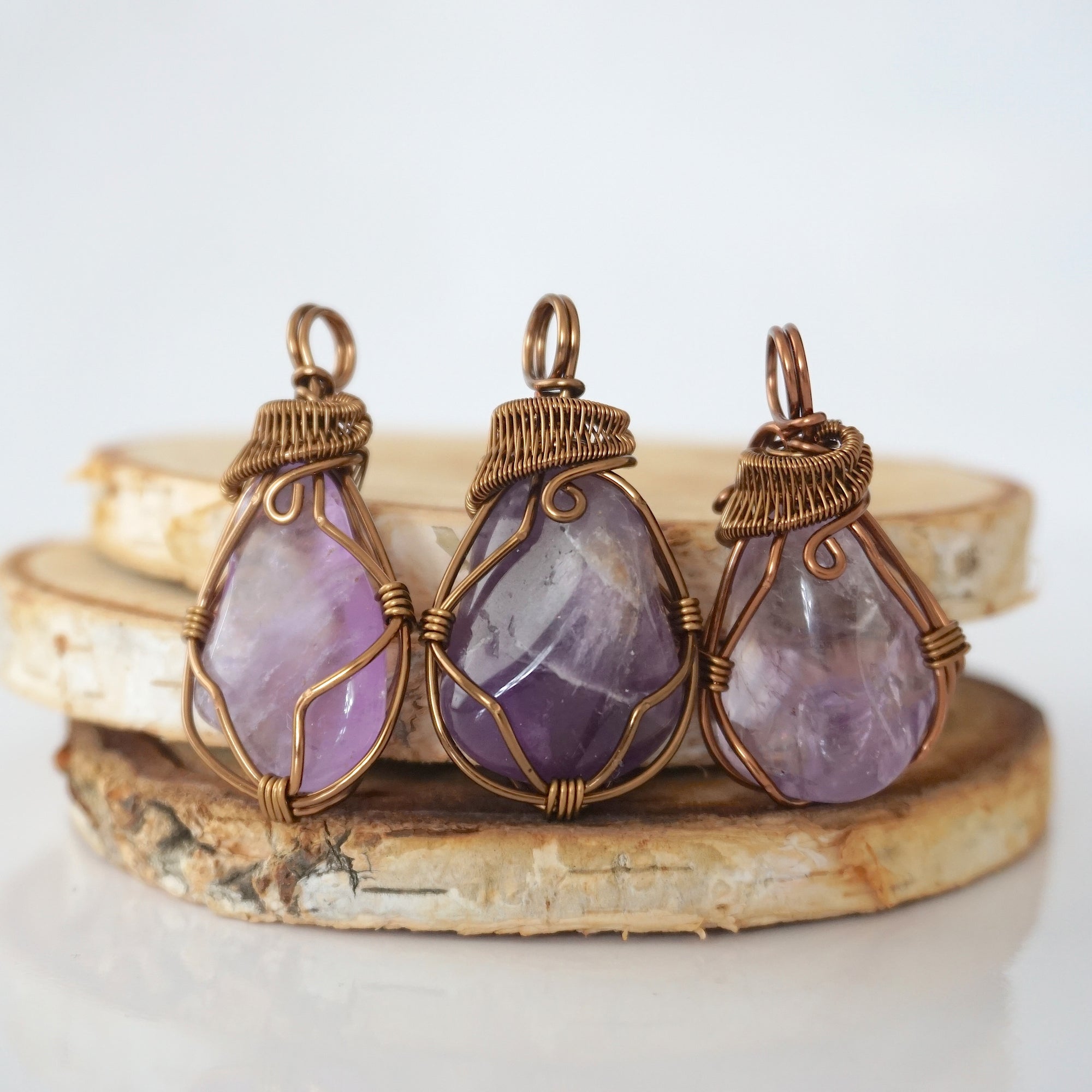 Multiple mens amethyst pendants showing natural variation in stone size, shape, and lavender colour — each one of a kind, February birthstone, bronze copper wire wrapped, Designs by Nature Gems