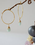 Close-up of handcrafted aquamarine hoop drop earrings in gold plated brass, featuring wire wrapped natural blue aquamarine gemstones on a jewelry display