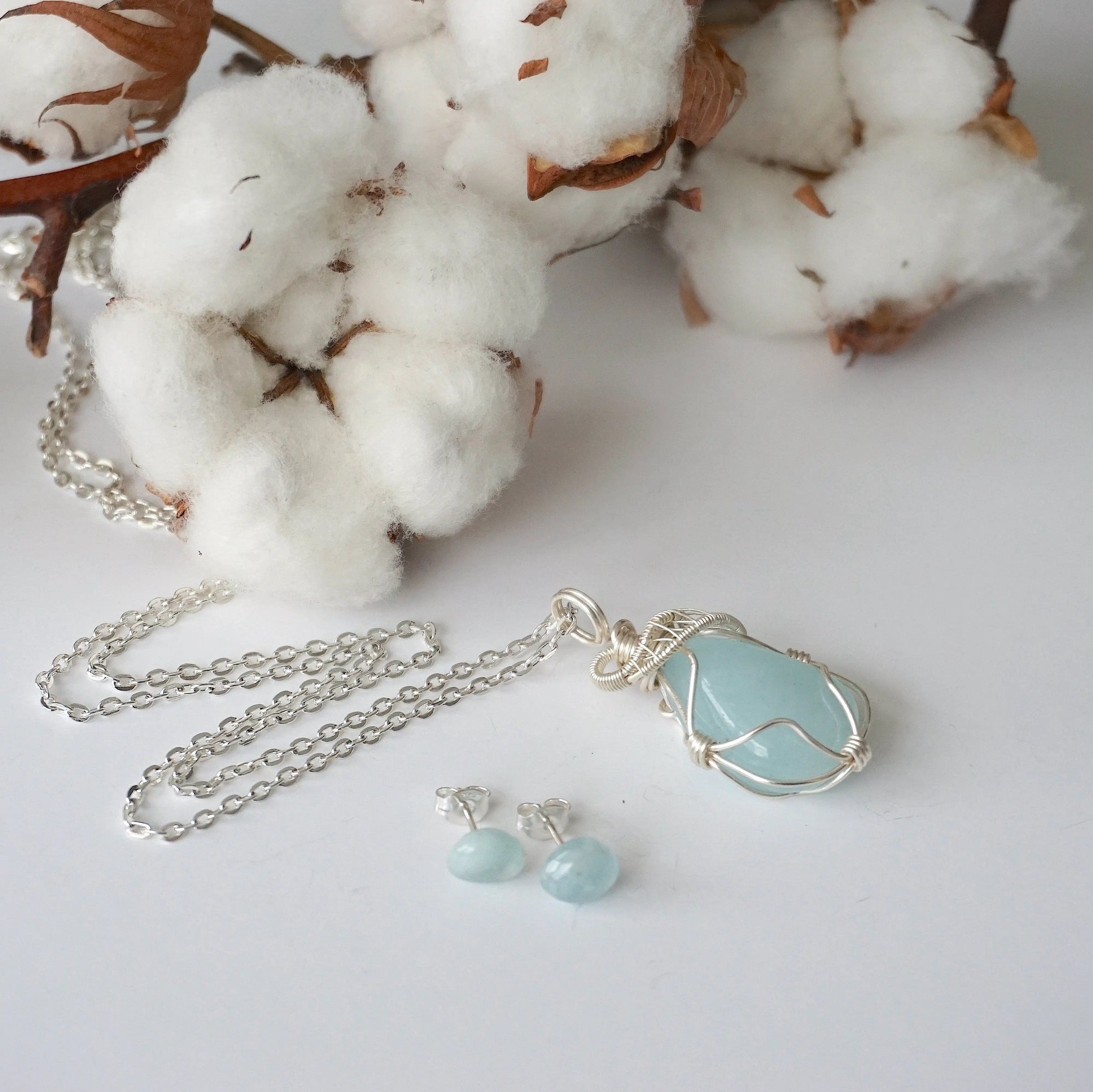 Aquamarine necklace and stud earrings laid flat, genuine aquamarine, artisan wire wrapped pendant, soft silver finish, sterling silver posts