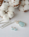 Aquamarine necklace and stud earrings laid flat, genuine aquamarine, artisan wire wrapped pendant, soft silver finish, sterling silver posts