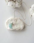 Aquamarine moon necklace laying flat, showing crescent shape and sterling silver chain, minimalist artisan design