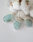 Three aquamarine pendants showing natural variation in size, shape, and blue color, artisan wire wrapped, soft silver over copper