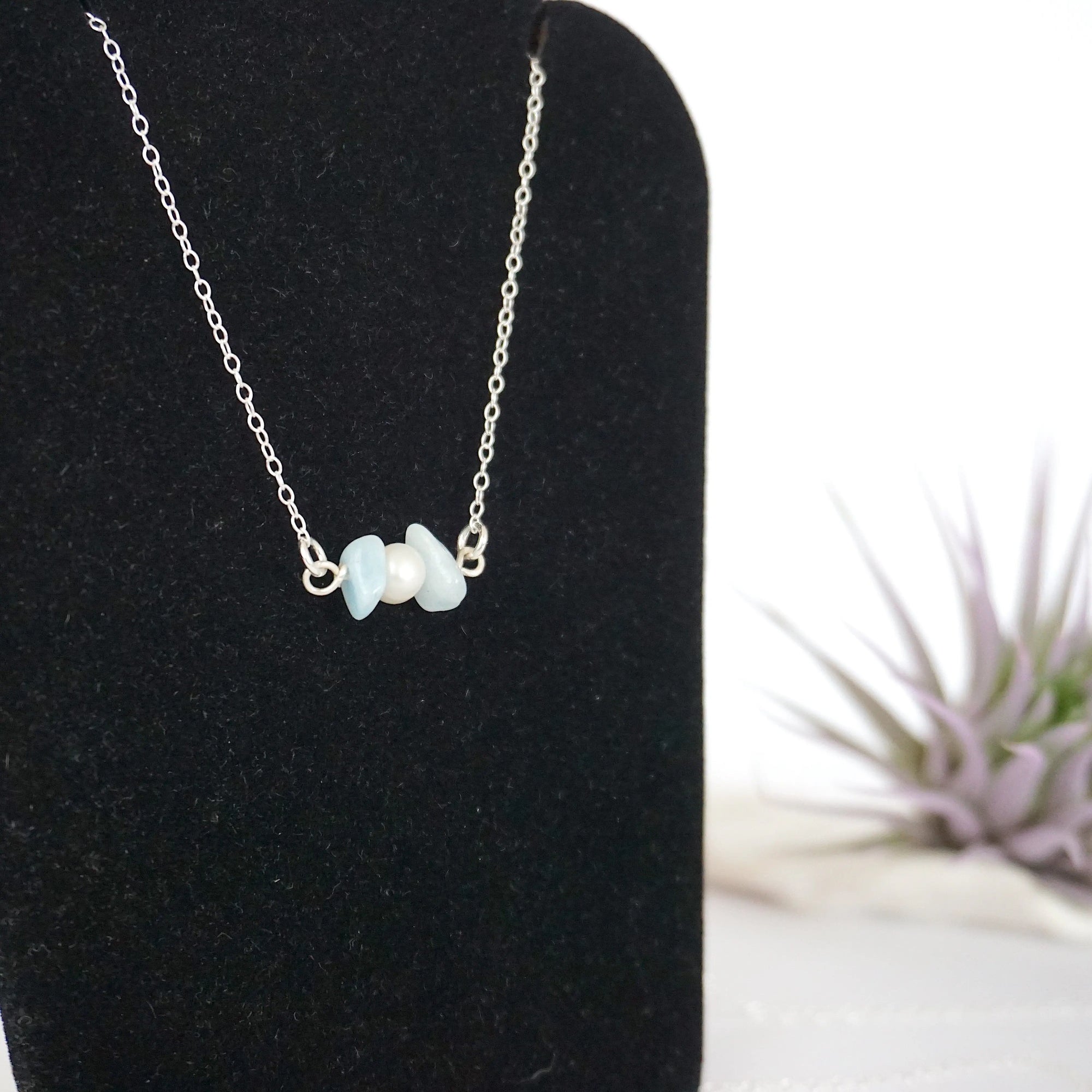 Focused left-side close-up of sterling silver aquamarine and pearl bar necklace on jewelry display