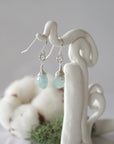 Side view of aquamarine sterling silver drop earrings showing wire wrapped natural faceted aquamarine, artisan craftsmanship, on a display – Designs by Nature Gems