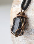 Left side angle detail of raw black tourmaline necklace on black leather cord, wire wrapped pendant by Designs by Nature Gems.