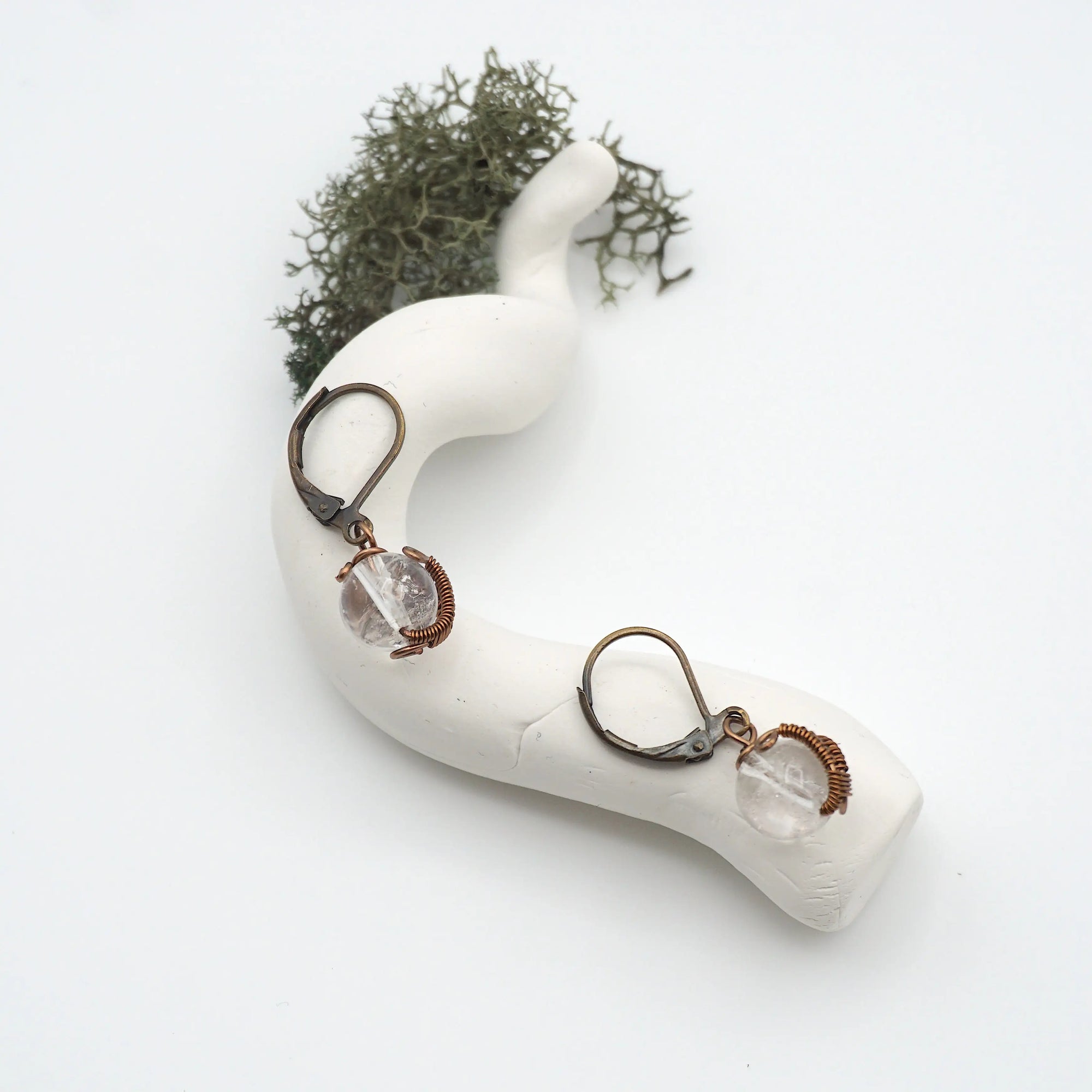 Bird’s eye view of clear quartz drop earrings laying flat on a display, showing detailed wire wrapping and gemstone clarity.