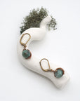 Bird’s eye view of emerald drop earrings laying flat on a display, showing detailed wire wrapping and gemstone color.