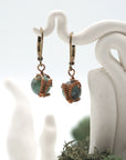 Close-up of handcrafted emerald drop earrings with antique bronze copper wire wrapping.