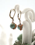 Side angle of emerald drop earrings on a display stand, highlighting antique bronze copper wire wrapping.