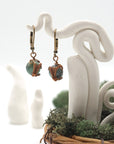 Front angle of emerald drop earrings hanging on a jewelry display, wire-wrapped design.