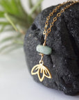Left angle detail of emerald and lotus necklace for women with natural faceted emerald bead and minimalist lotus charm