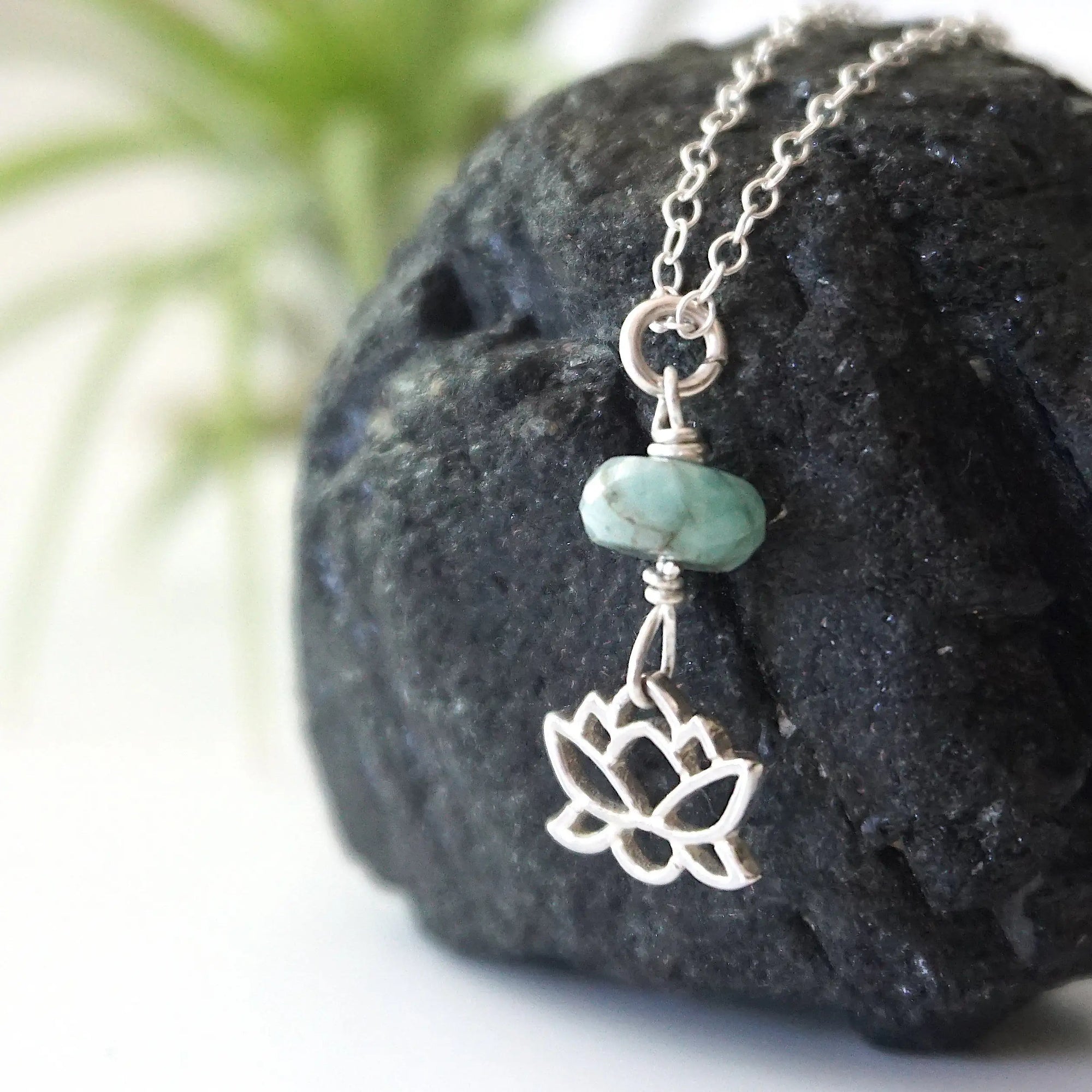 Left angle detail of emerald and lotus necklace for women with natural faceted emerald bead and minimalist lotus charm