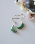 Emerald moon drop earrings in 925 sterling silver displayed on a flat surface with natural faceted crescent moon emeralds.