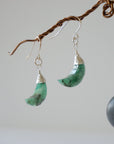 Side angle view of emerald moon drop earrings showing sterling silver artisan wire wrapping and faceted emerald detail.