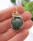 Emerald pendant necklace for women shown in hand for size reference with natural polished-raw emerald in 14k gold filled and sterling silver wire wrapping