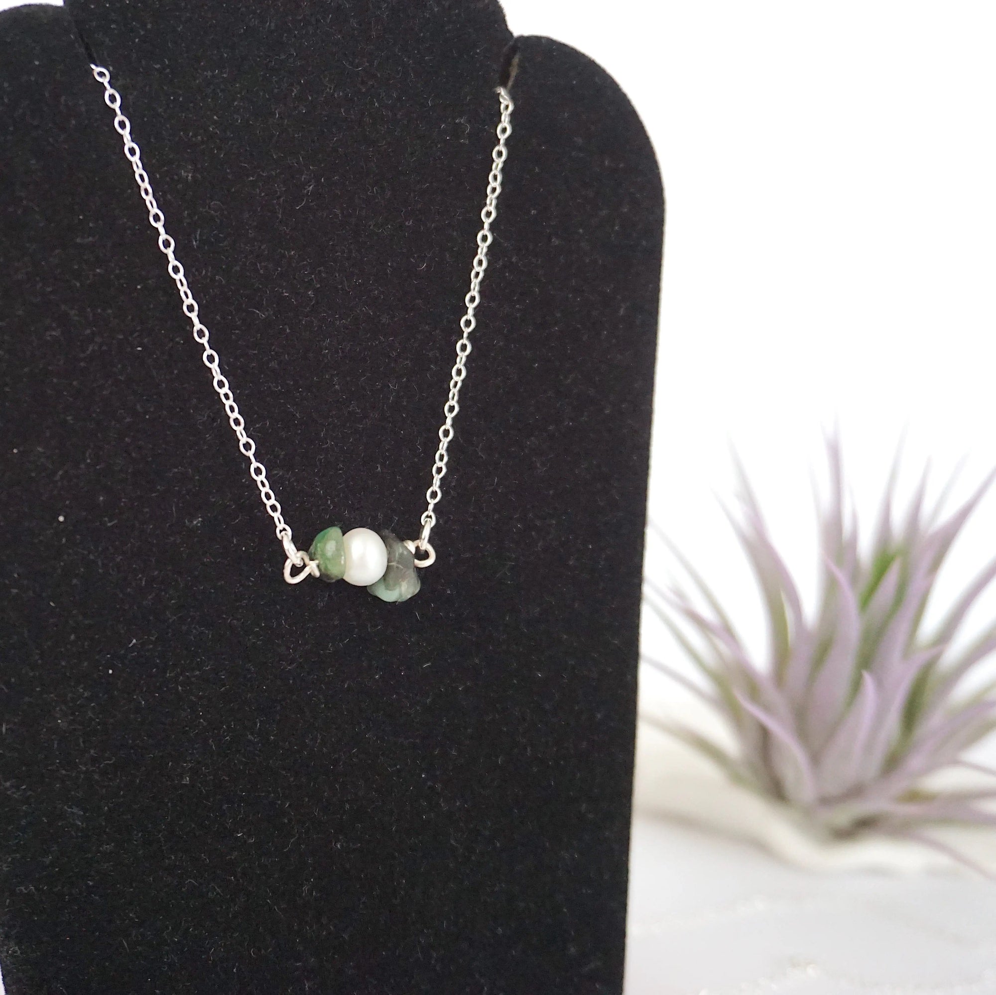 Focused left-side close-up of sterling silver emerald and pearl bar necklace on jewelry display