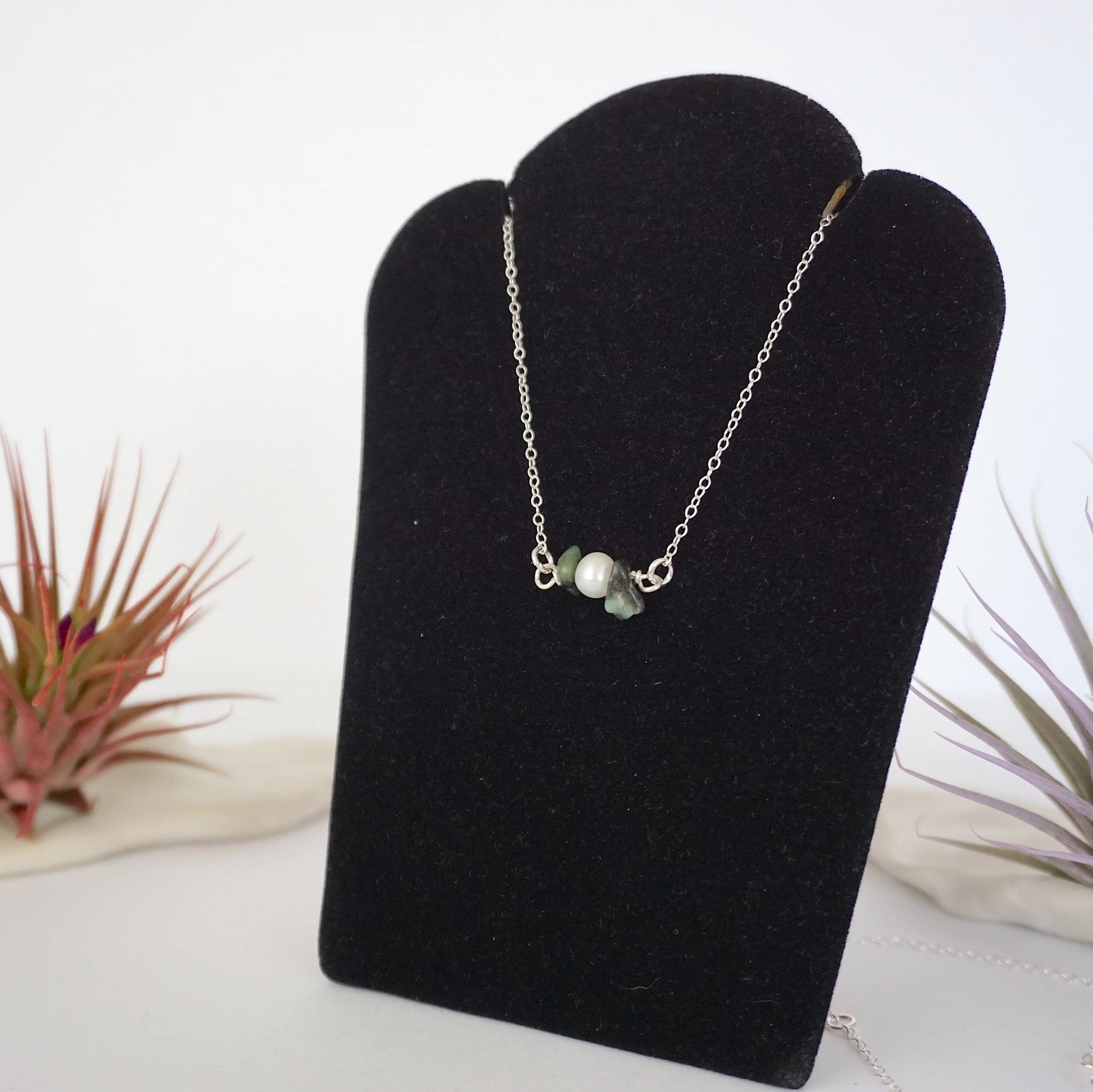 Left angle view of emerald and pearl bar necklace in 925 sterling silver on jewelry display