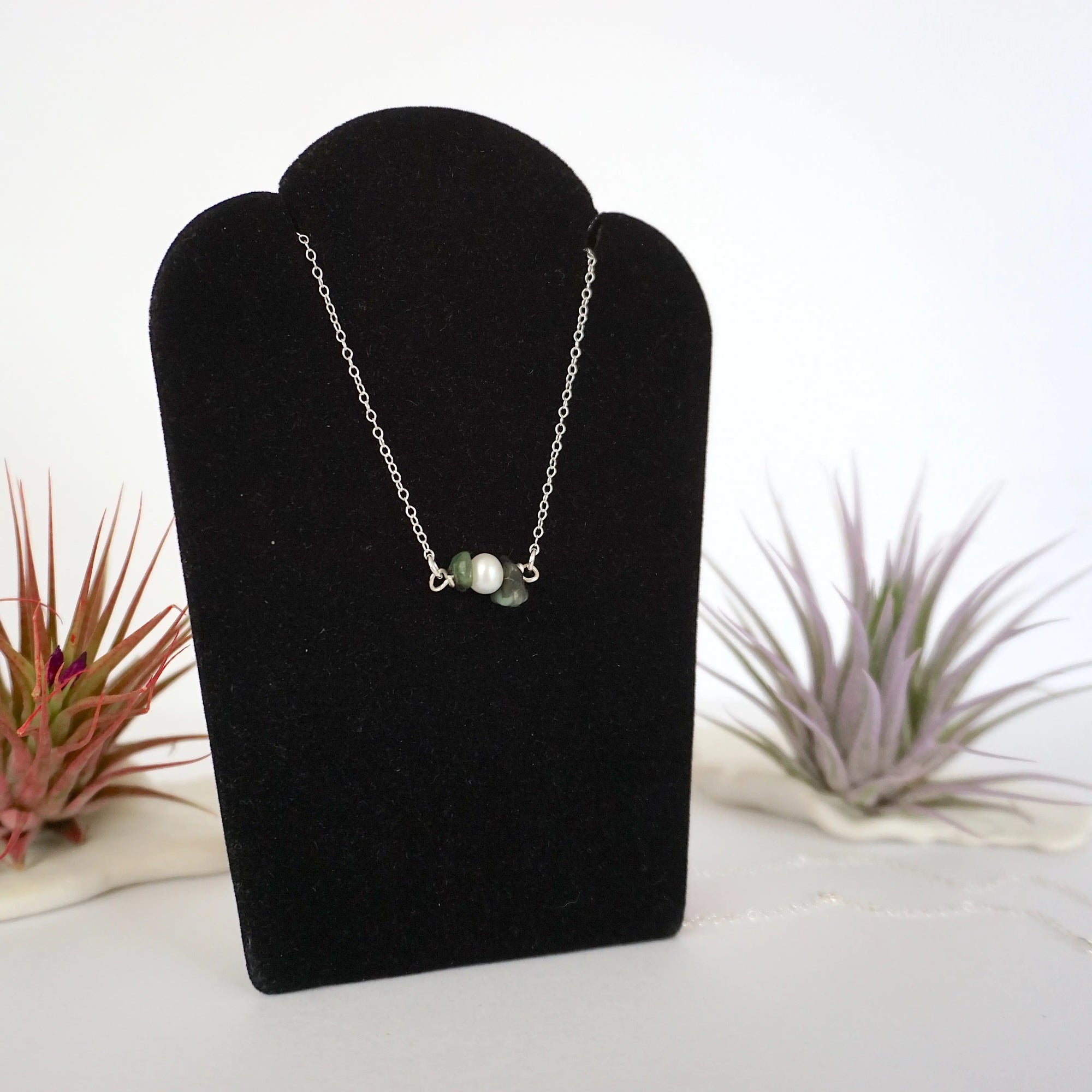 Right angle view of emerald and freshwater pearl bar necklace in 925 sterling silver on jewelry display