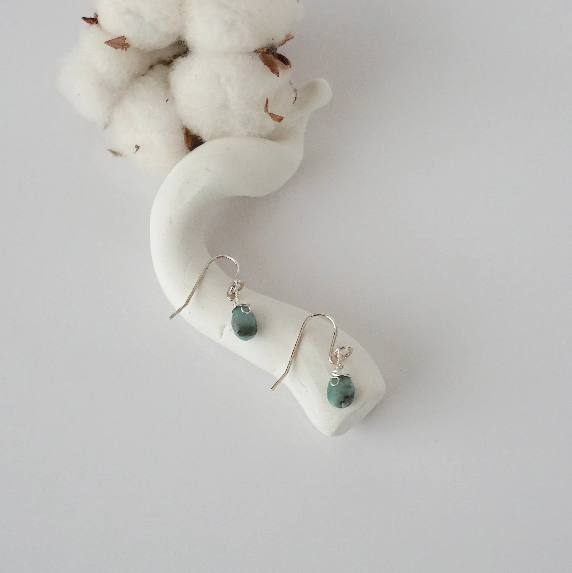 Emerald sterling silver drop earrings with faceted natural emerald stones and wire wrapping, laying flat on a display – Designs by Nature Gems
