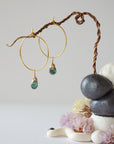 Angled close detail of faceted emerald hoop drop earrings showing artisan wire wrapping in warm gold copper