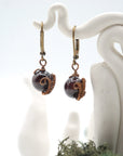 Close-up view of handcrafted natural garnet drop earrings with antique bronze copper wire wrapping.