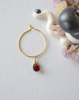 Flat lay of a gold plated garnet hoop drop earring, highlighting the wire wrapped natural garnet gemstone and minimalist hoop design