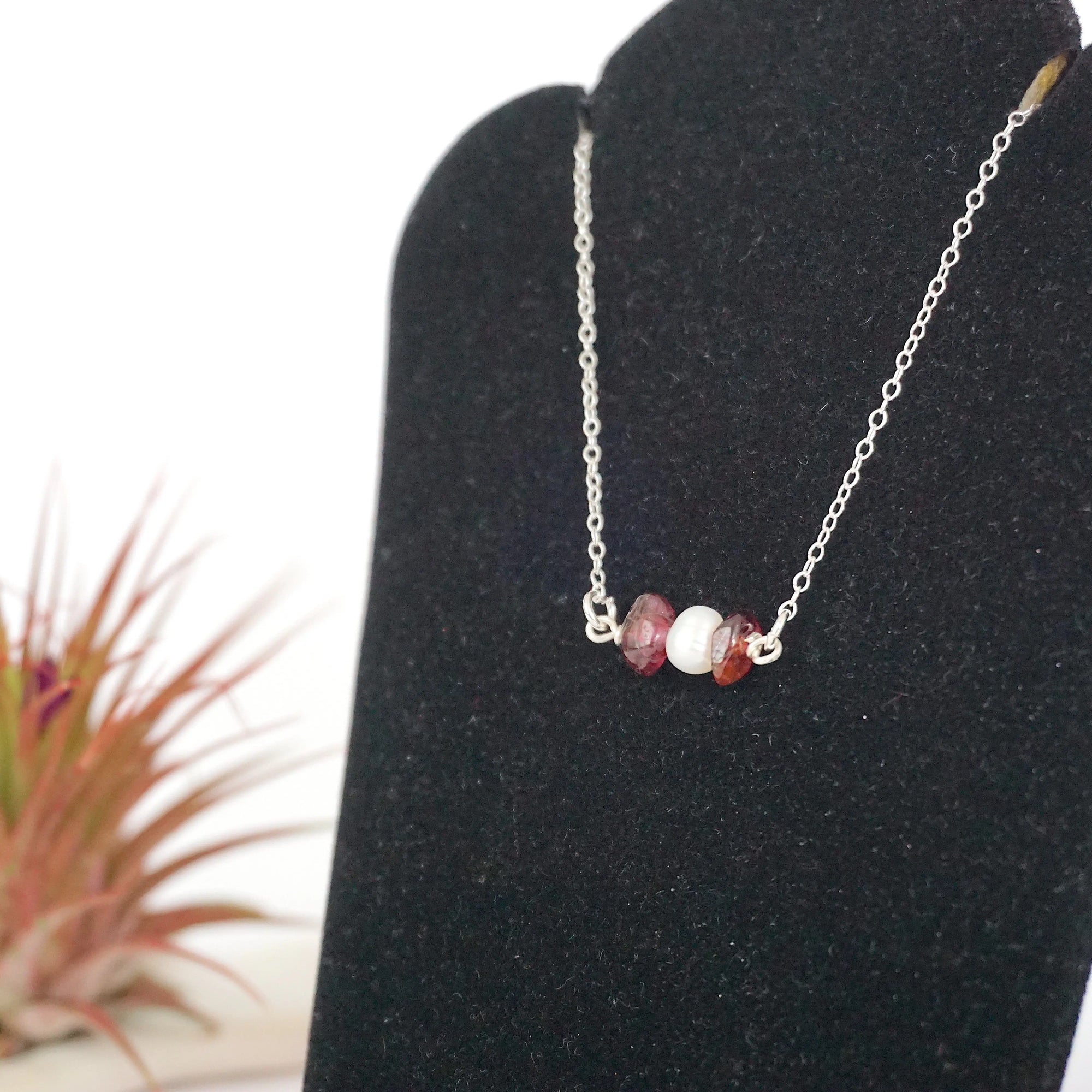 Focused left-side close-up of sterling silver garnet and pearl bar necklace on jewelry display