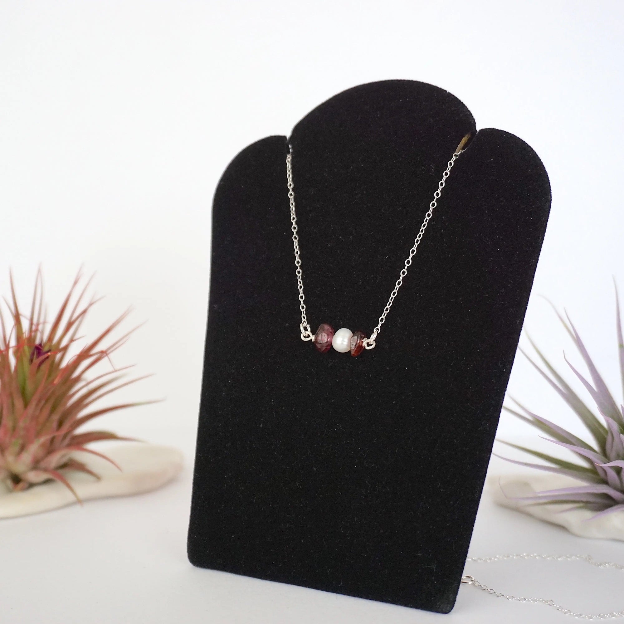 Left angle view of garnet and pearl bar necklace in 925 sterling silver on jewelry display