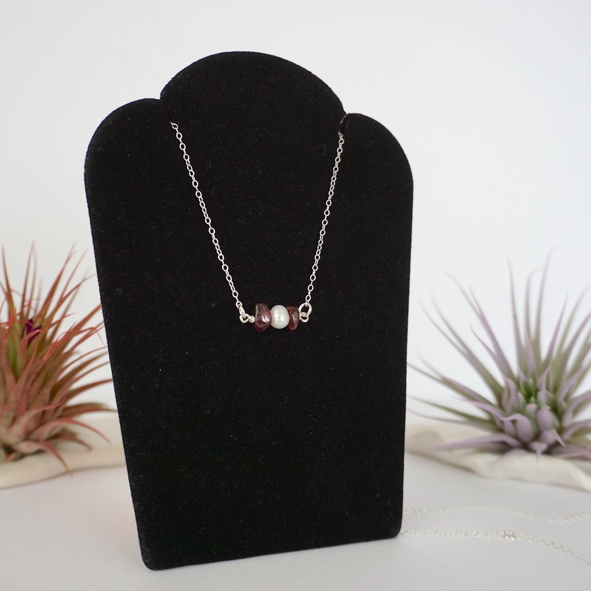 Right angle view of garnet and freshwater pearl bar necklace in 925 sterling silver on jewelry display