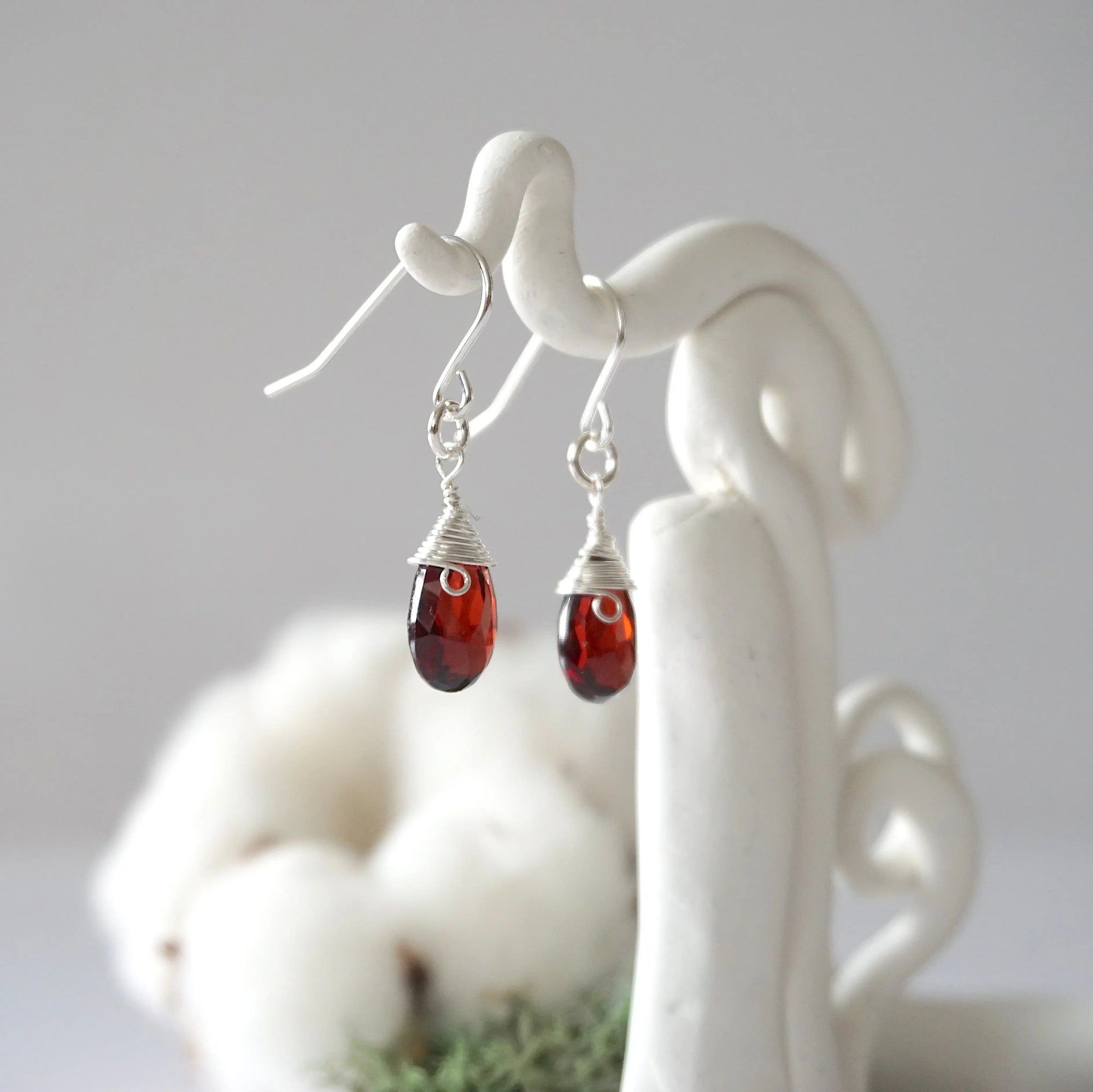 Side view of sterling silver garnet drop earrings showing wire wrapped natural faceted garnet, artisan craftsmanship, on a display – Designs by Nature Gems