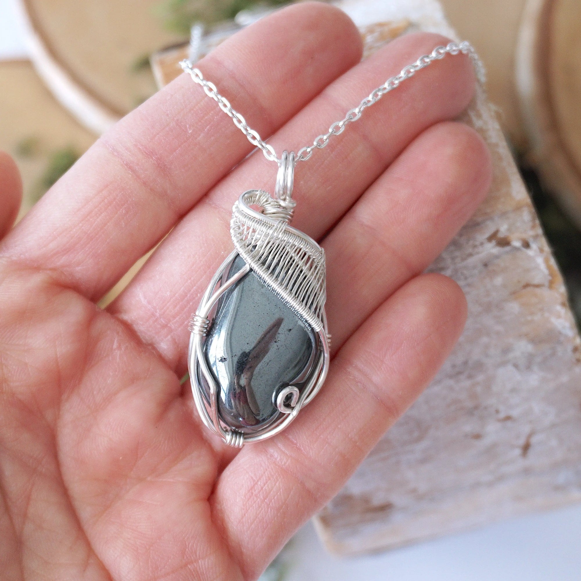 Natural hematite pendant shown in hand for size reference with handcrafted soft silver over copper wire wrap necklace