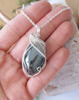 Natural hematite pendant shown in hand for size reference with handcrafted soft silver over copper wire wrap necklace